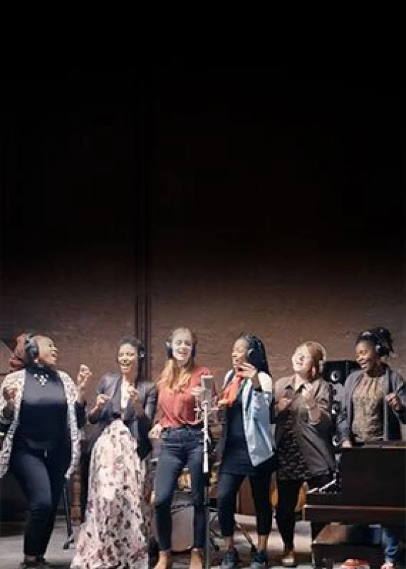 A group of female artists singing in a microphone