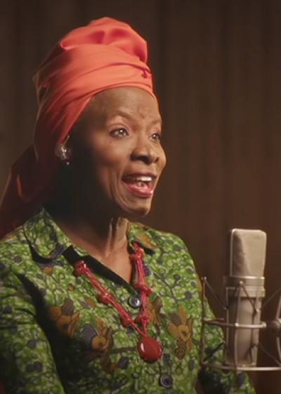Angelique Kidjo in front of a microphone performing 